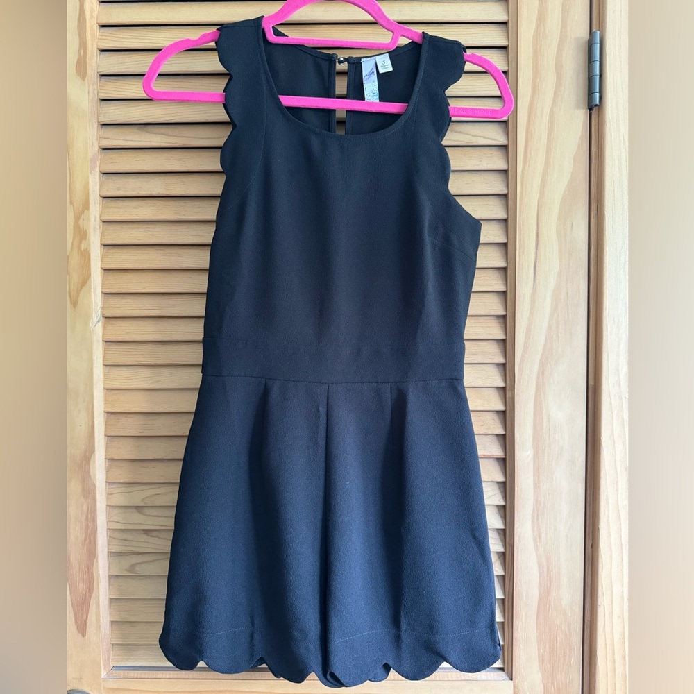 Black sleeveless romper with scalloped edges.